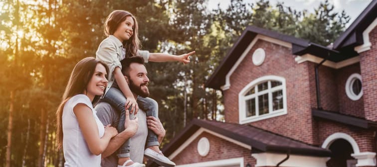 Happy family is standing near their modern house and smiling.