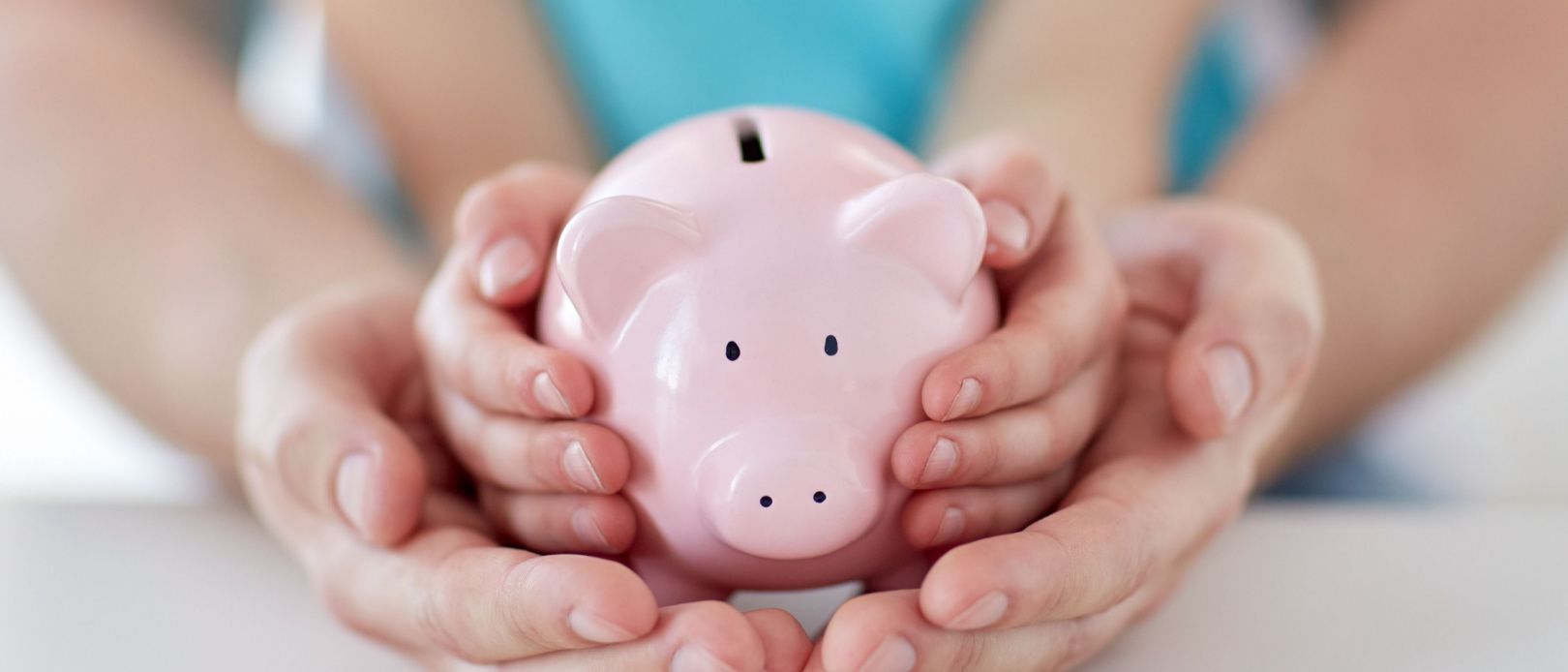  Close up of father and daughter hands holding pink piggy bank