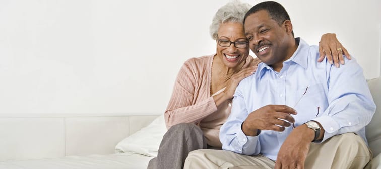 A retirement-aged couple smile on the couch.