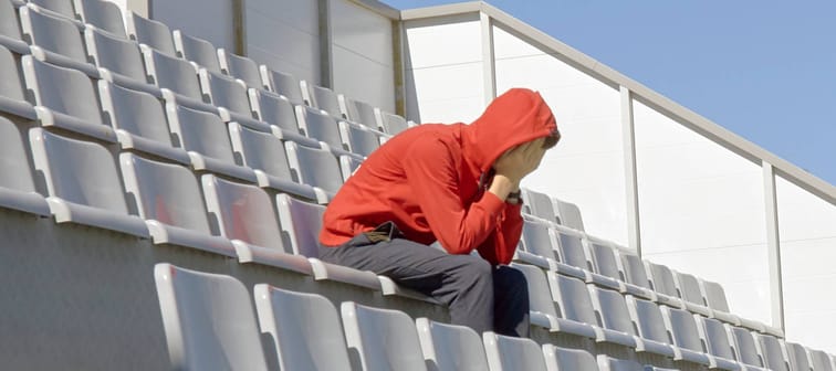 Fan sits in empty stands, hands over face sad