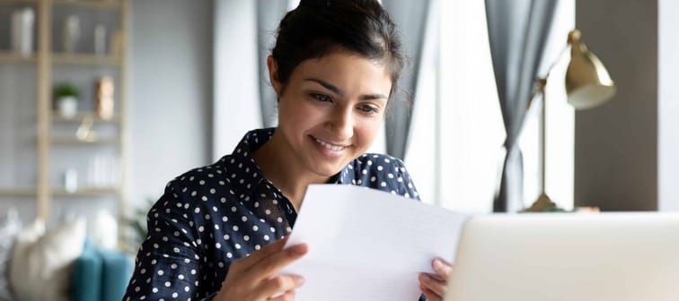 Smiling young woman holding paper while sitting in front of a laptop,